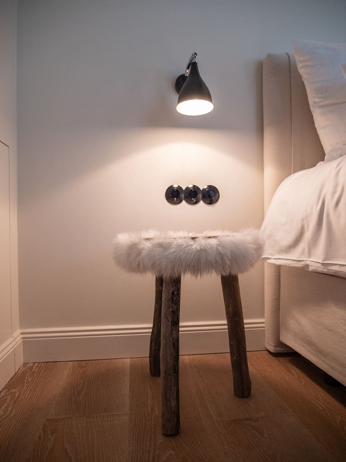 Fell-Hocker neben dem Bett unter einer Wandleuchte