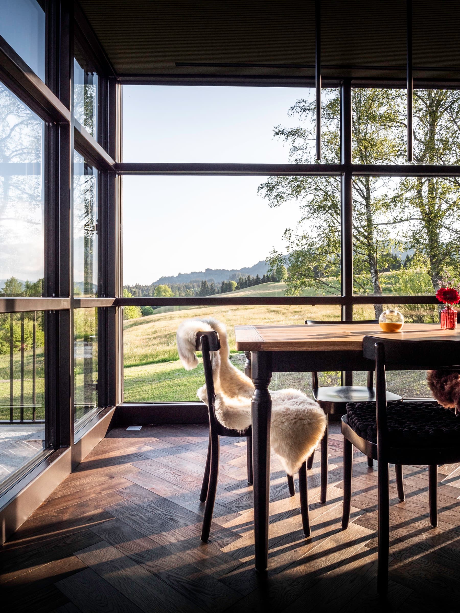 Alpenloge – Esstisch mit Stühlen und Schafsfellen vor der Glasfront mit Blick in die Allgäuer Landschaft