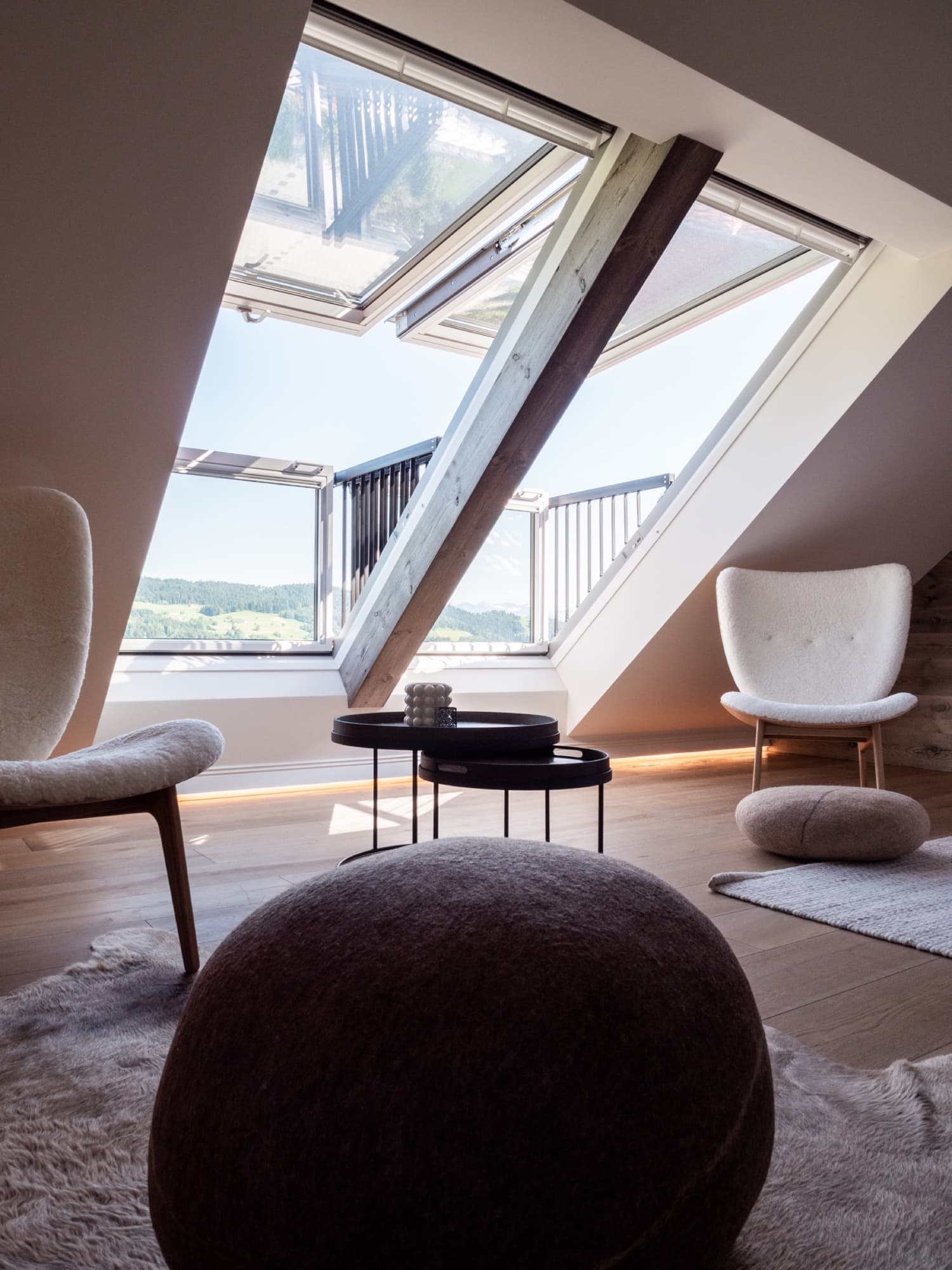 Alpenloge – Dachzimmer mit geöffneten Dachfenstern zum Balkon, Schaffell-Sesseln und Blick auf die Allgäuer Hügel